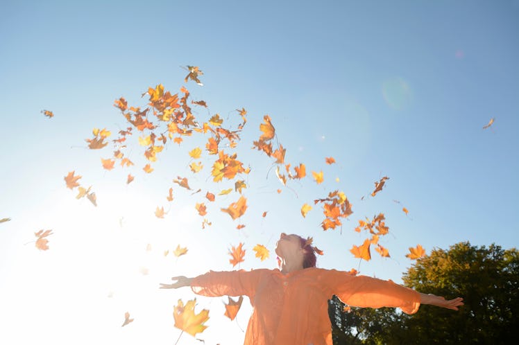 Young woman throwing autumn leaves in the air
