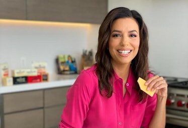 Eva Longoria poses with a piece of cheese while standing in her kitchen.