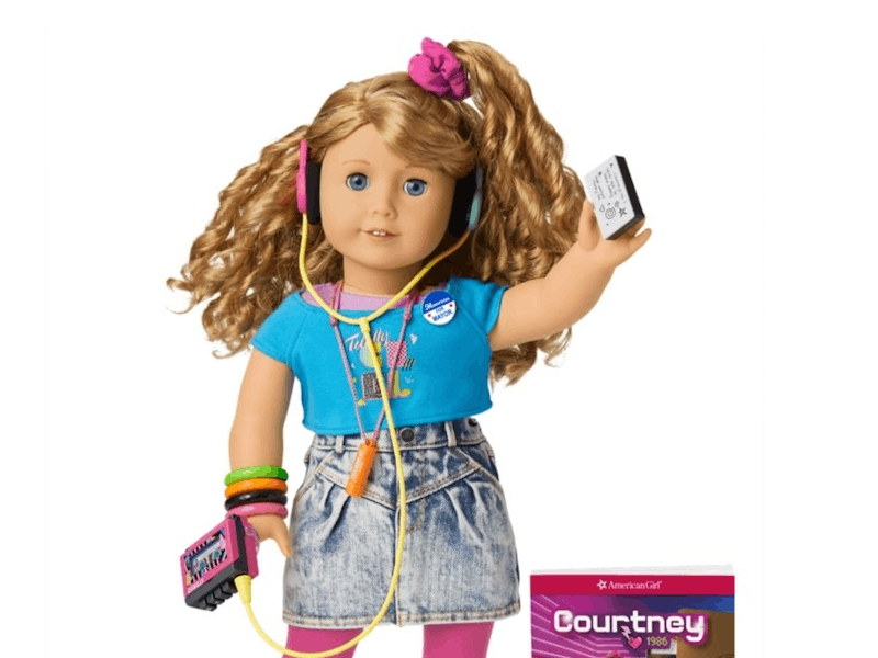 An American Girl named Courtney can be seen with a blue shirt, faded shorts, pink socks, white shoes...