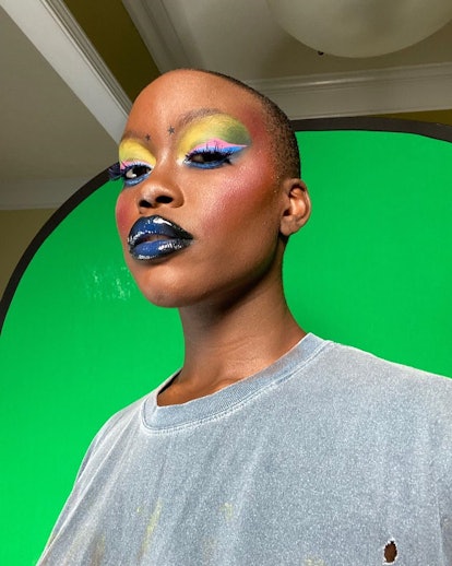 A model in front of a green screen with highly colorful makeup and a grey shirt