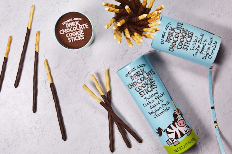 Trader Joe's Dark Chocolate Cookie Sticks are laid out on a concrete table with the canisters they c...