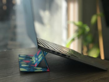 A side photo of the Moft laptop stand on a dining table. The background shows glass window for a pat...