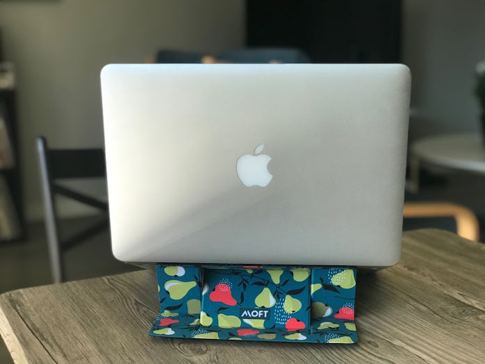A Macbook can be seen resting on top of a light green, teal blue, and blue colored laptop stand with...