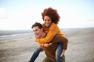 Young couple piggybacking on beach in sweaters