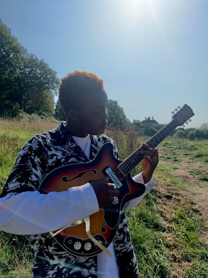 London-based singer Arlo Parks playing a guitar outdoors 