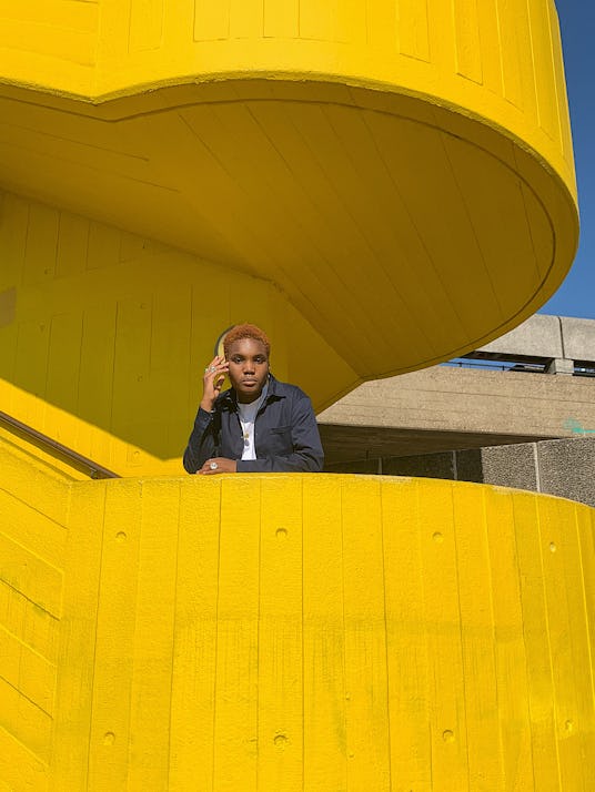London-based singer Arlo Parks posing on a staircase of a bright yellow building