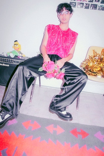 Curtis Waters in black satin pants and a pink shirt, sitting on a table