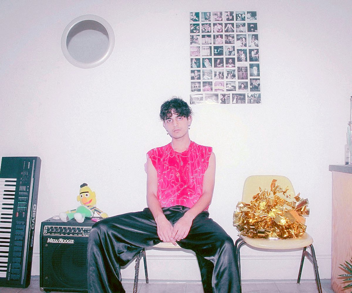 Curtis Waters sitting in his living room in black satin pants and a pink shirt