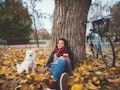 Young woman relaxing in fall leaves with dog and bike