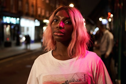 Michaela Coel in a white shirt standing in the middle of a street during night time