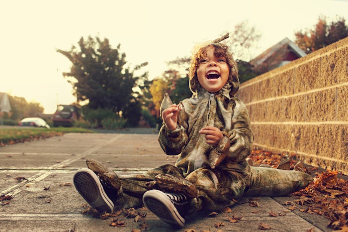 little boy in dinosaur halloween costume sitting on street