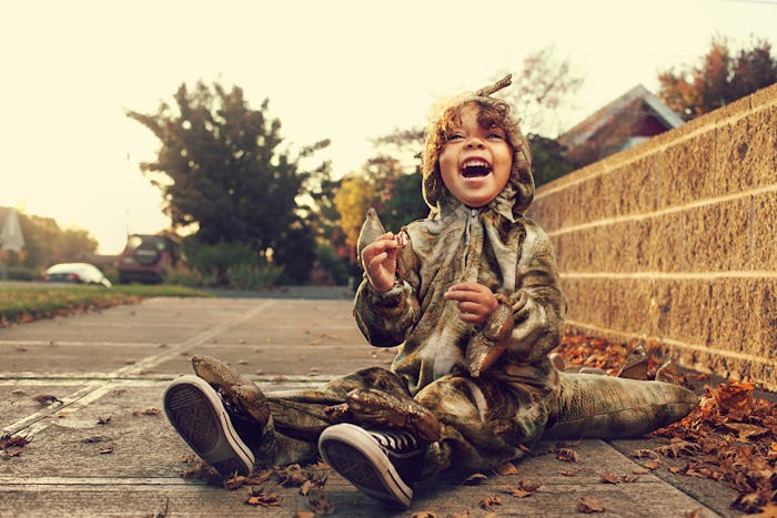 little boy in dinosaur halloween costume sitting on street