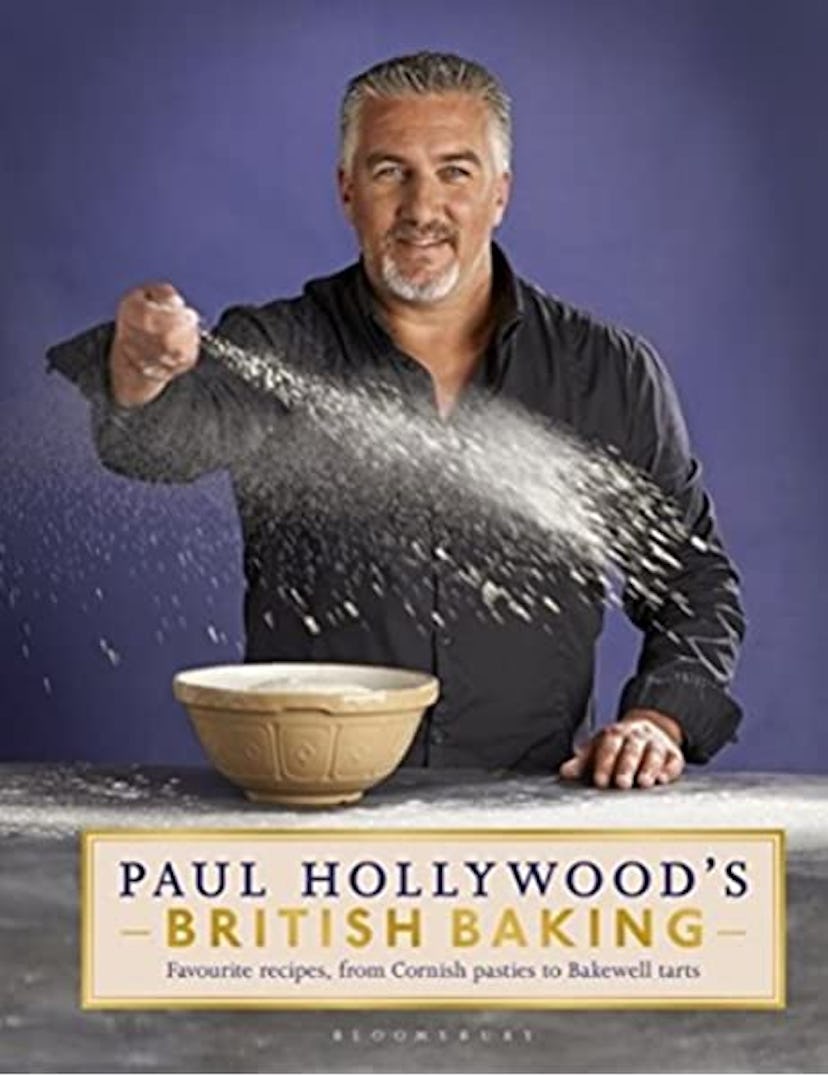 Paul Hollywood poses wearing a black shirt with a bowl of flour. He's dashing a fistful of the flour...