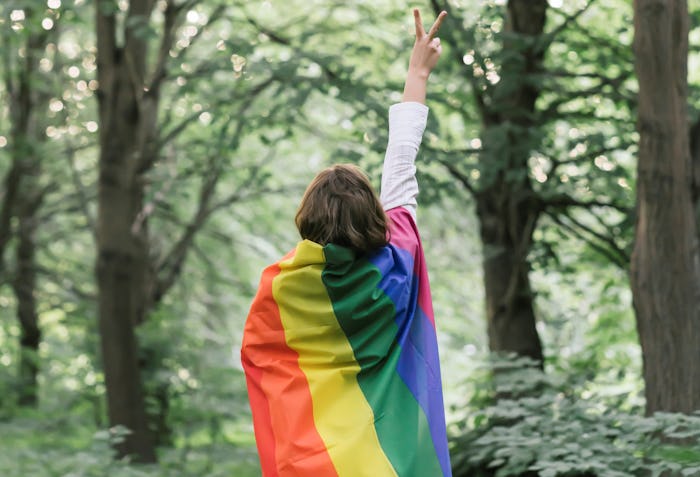 woman wrapped in rainbow flag giving peace sign in the woods