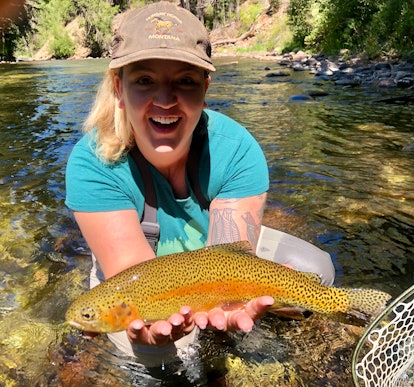 Ali Wunderman standing in the middle of a river showing the fish she caught while fly fishing