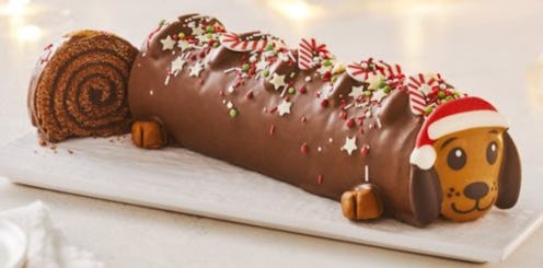 A Sainsbury's sausage dog yule log cake can be seen on a white plate. A slice has been taken from th...