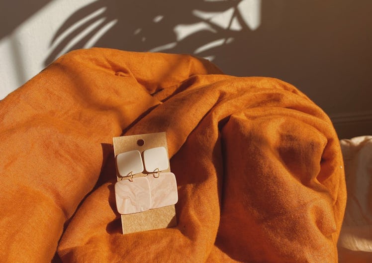 A pair of Bohemian polymer clay earrings sit on an orange blanket next to the shadow of a palm leaf.