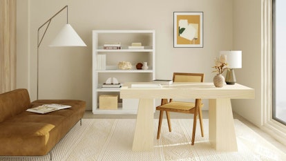 A decorated home office has minimalist feel with a white bookshelf and wooden desk. 