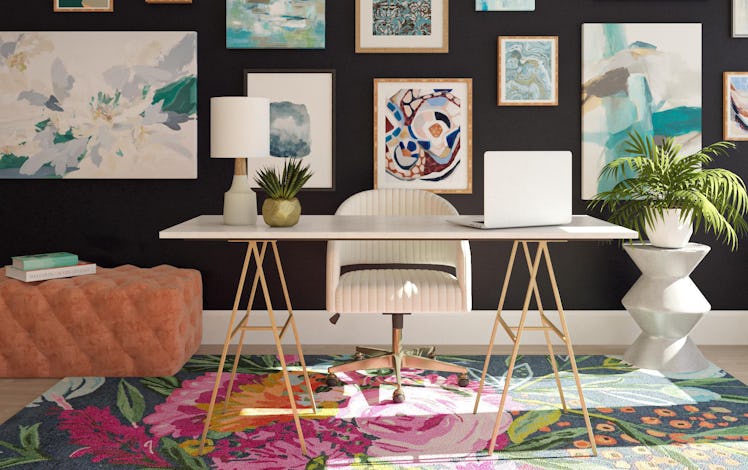 A decorated home office has a colorful rug and artwork hung all over the wall.