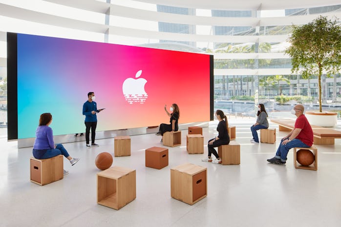 People watch a large projection screen with the Apple logo.