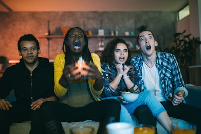 Young scared friends watching horror movie on TV at home, their zodiac sign's favorite thing about f...