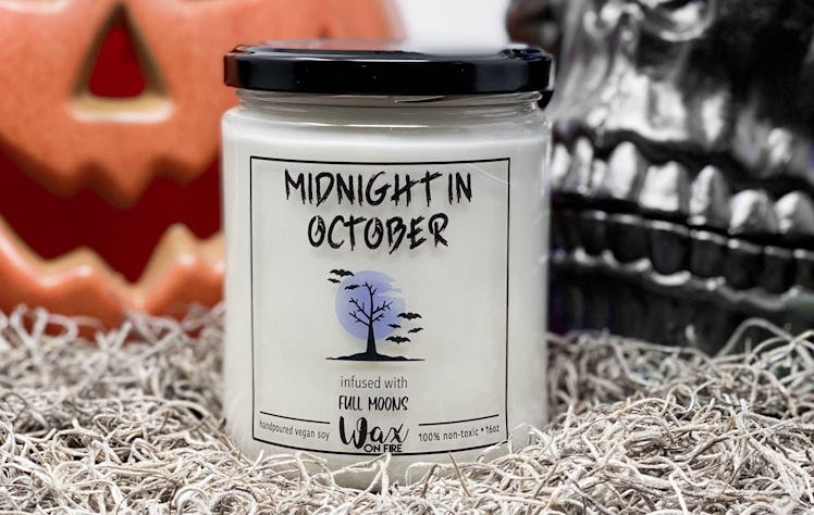 A Halloween themed candle sits in front of a pumpkin and skull.