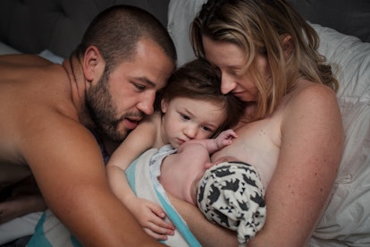 mother father and older child looking at new baby as it breastfeeds