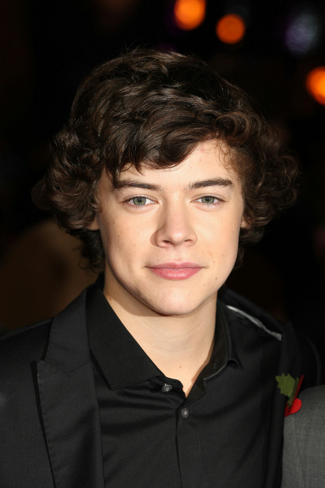 A young Harry Styles wears a black button down top with curly hair