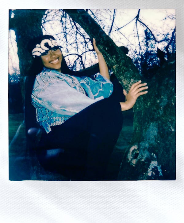 Jazmine Sullivan in a denim jacket is crouching and holding onto a tree