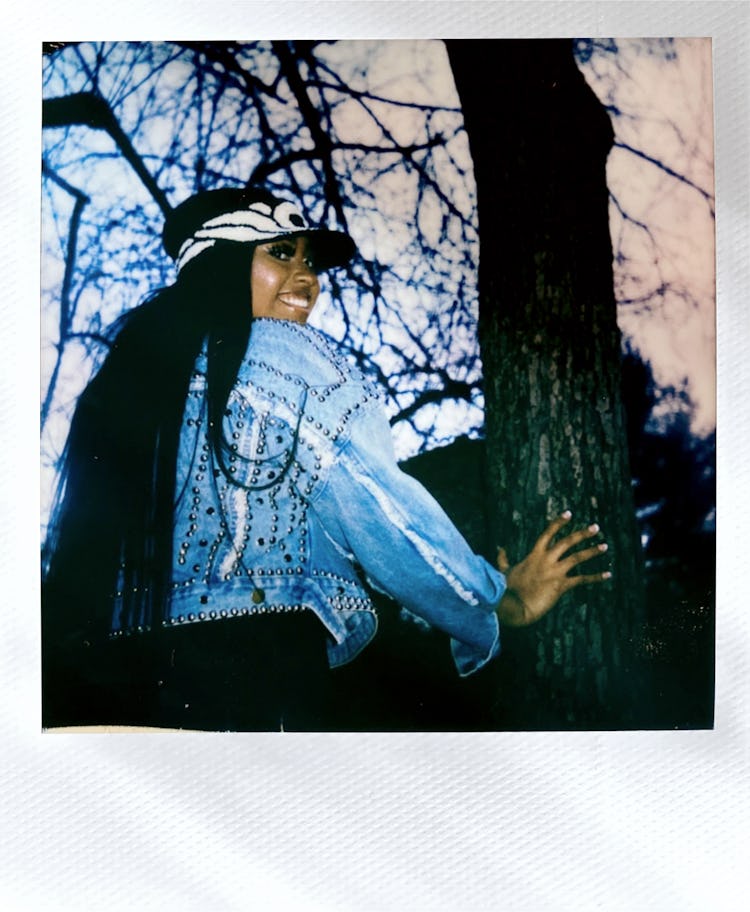Jazmine Sullivan in a denim jacket, smiling and touching a tree 