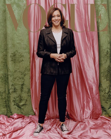 Kamala Harris posing for vogue in a black blazer a grey shirt and sneakers, in front of a pink curta...