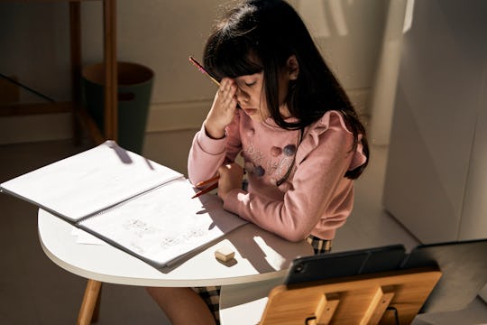 Girl with long brown hair sits at a small table with a notebook, looking tired