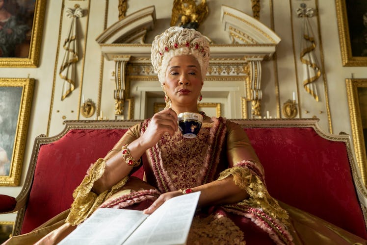 Queen Charlotte from 'Bridgerton' sips tea and holds Lady Whistledown's paper while sitting on a thr...