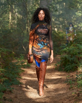 A curly model walking the woods in an earthy-toned tie-dye dress, wearing a banana crossbody by Burb...