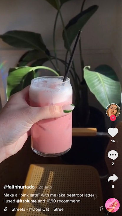 A woman holds up a pink beetroot latte drink for TikTok. 