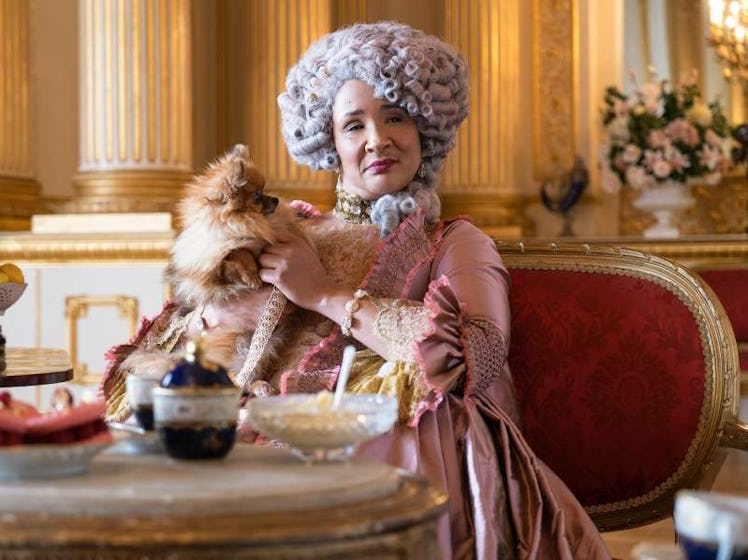 Queen Charlotte from 'Bridgerton' holds her dog and sits in a regal chair while enjoying afternoon t...