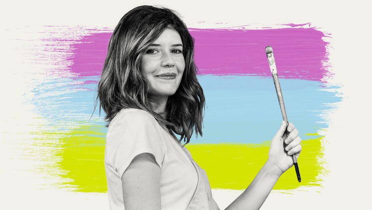 Artist Lourdes Villagomez stands in profile, holding up a paintbrush against a background of three b...