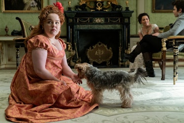Penelop Featherington from 'Bridgerton' sits on the floor with a dog, while Marina and Colin talk. 