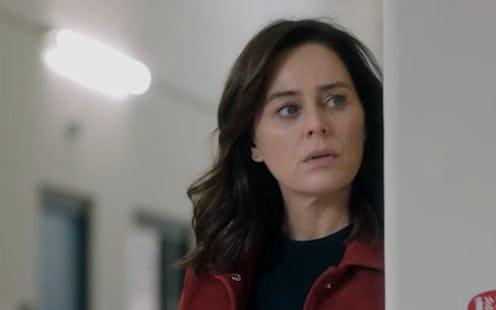 Jill Halfpenny looks round a door suspiciously. She's wearing a red coat and black top