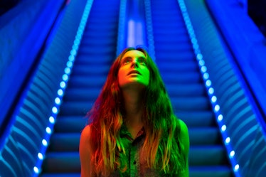 Portrait of illuminated young woman in front of blue lighted escalator looking up