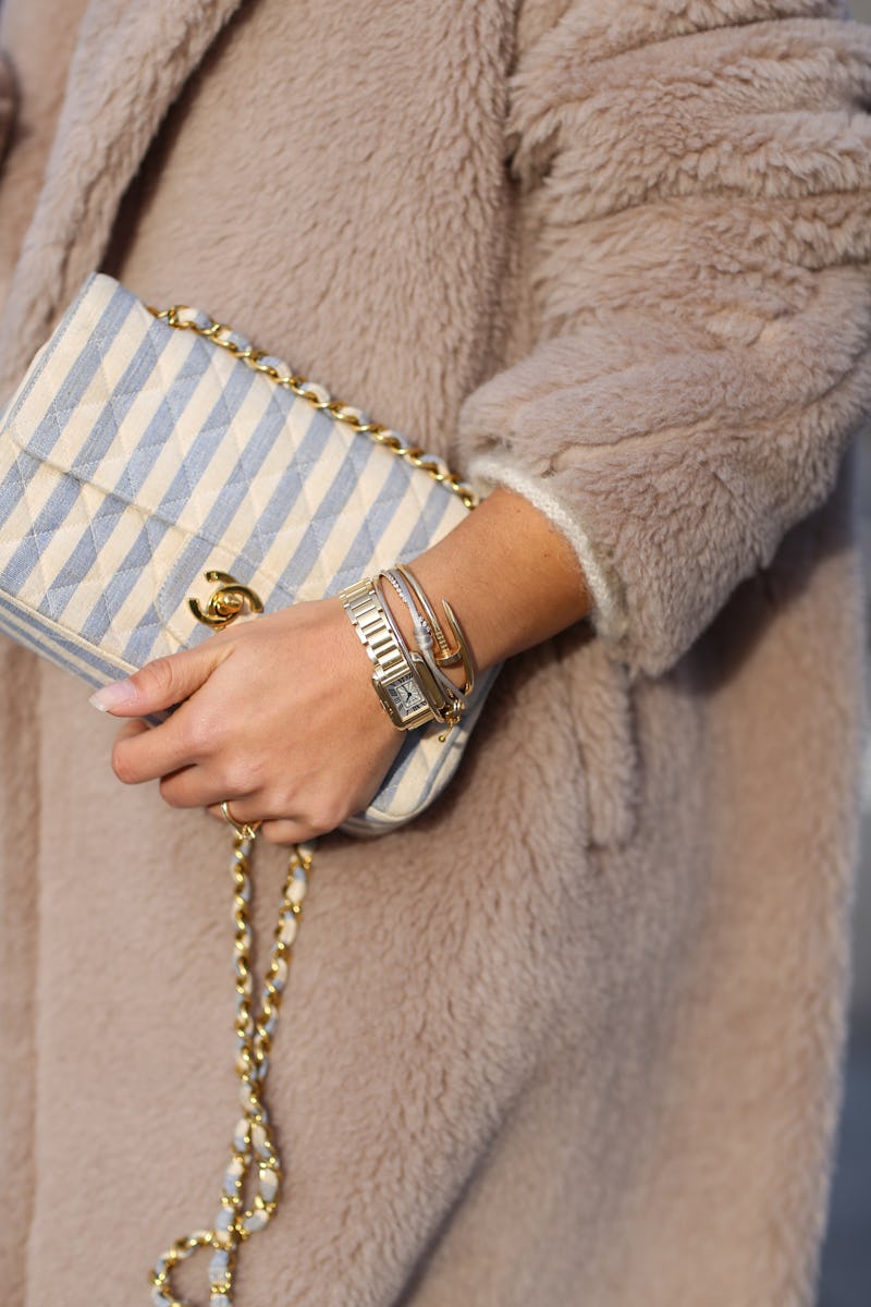 Person wearing a furry coat, holding a Chanel bag and wearing a wristwatch.