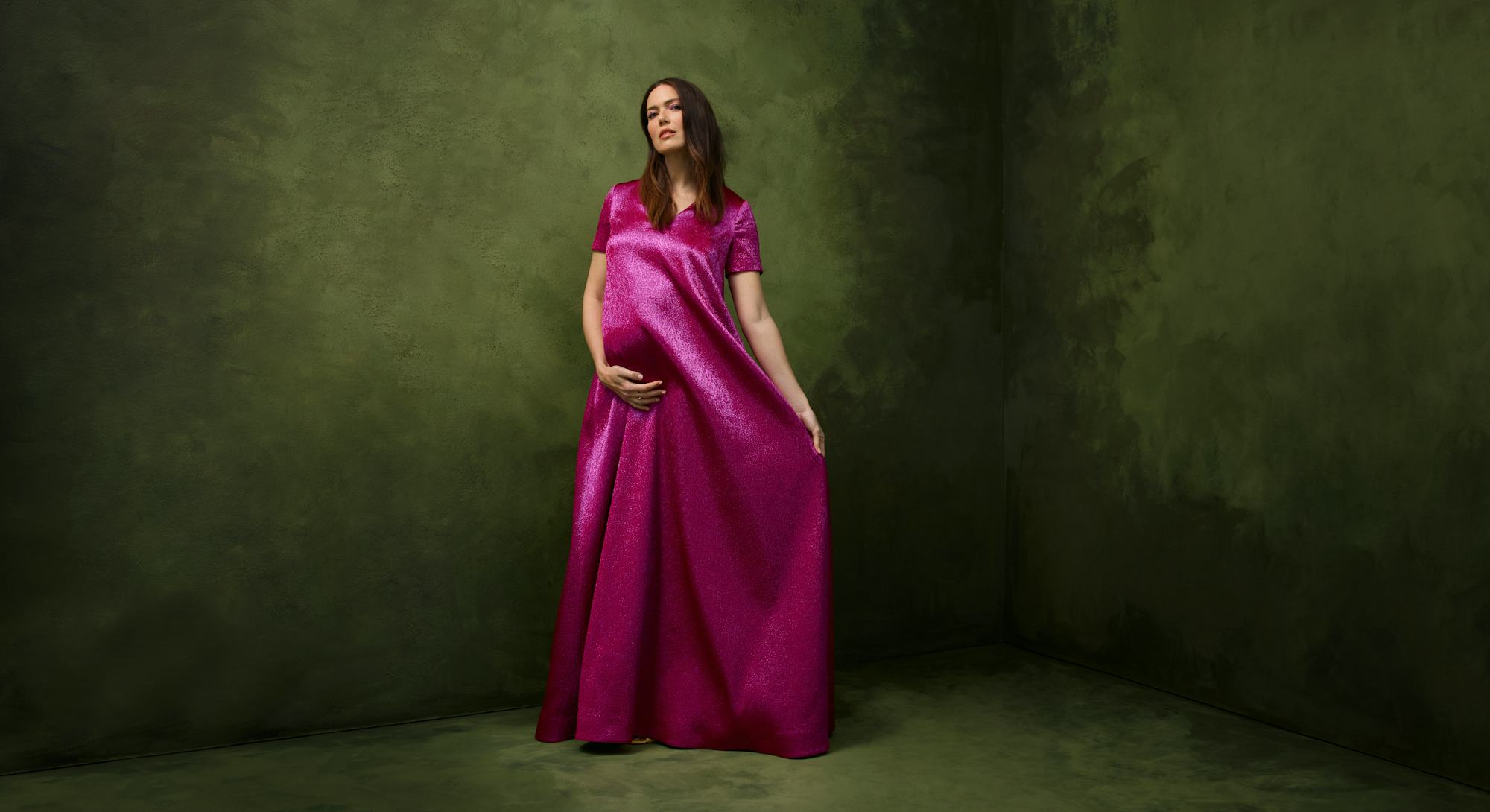 Mandy Moore wearing a long satin magenta dress while posing for her pregnancy photos