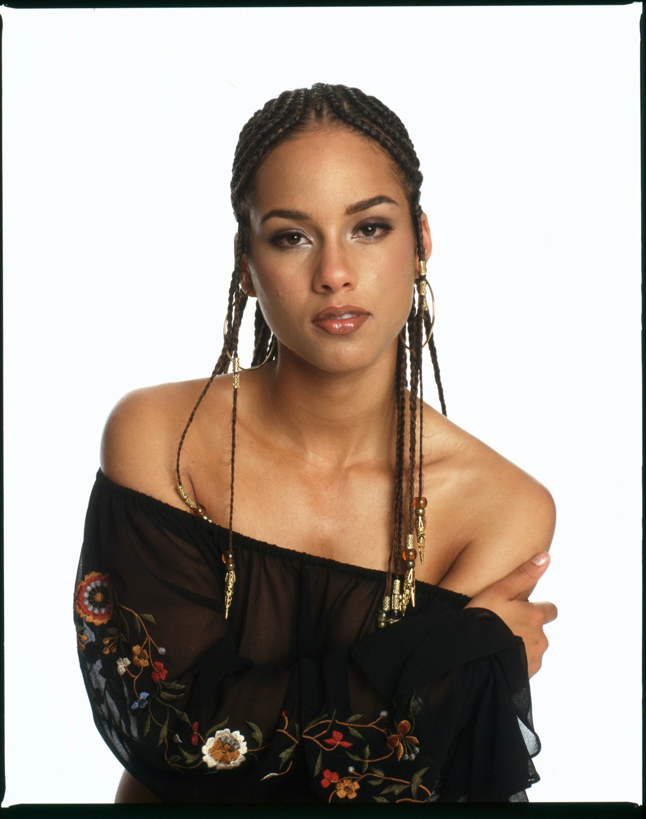 Alicia Keys, her hand on her shoulder, poses in a top, braids hanging down below her shoulders