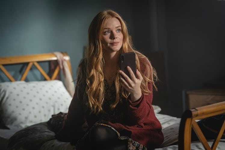 Bloom smiles at her phone in a red cardigan. 