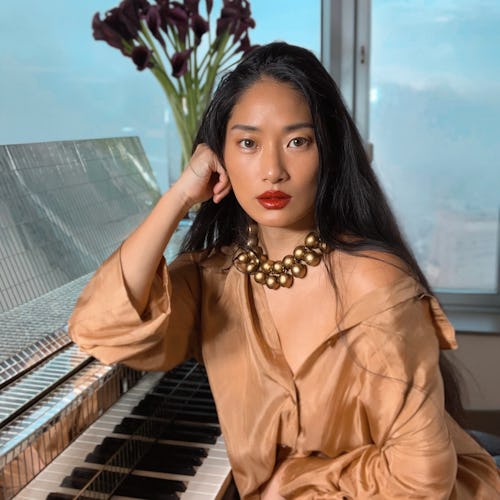 The pianist and composer Chloe Flower, posing in a brown satin dress accessorized with a necklace ma...