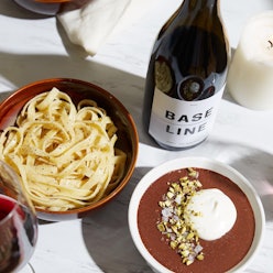 A bowl with pasta, a bowl with a dip, and a bottle of wine to make Valentine's Day feel romantic at ...