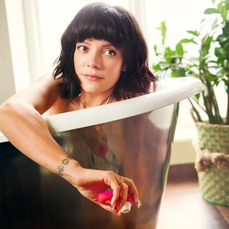 Singer Lily Allen poses in a tub holding a pink and orange Womanizer sex toy