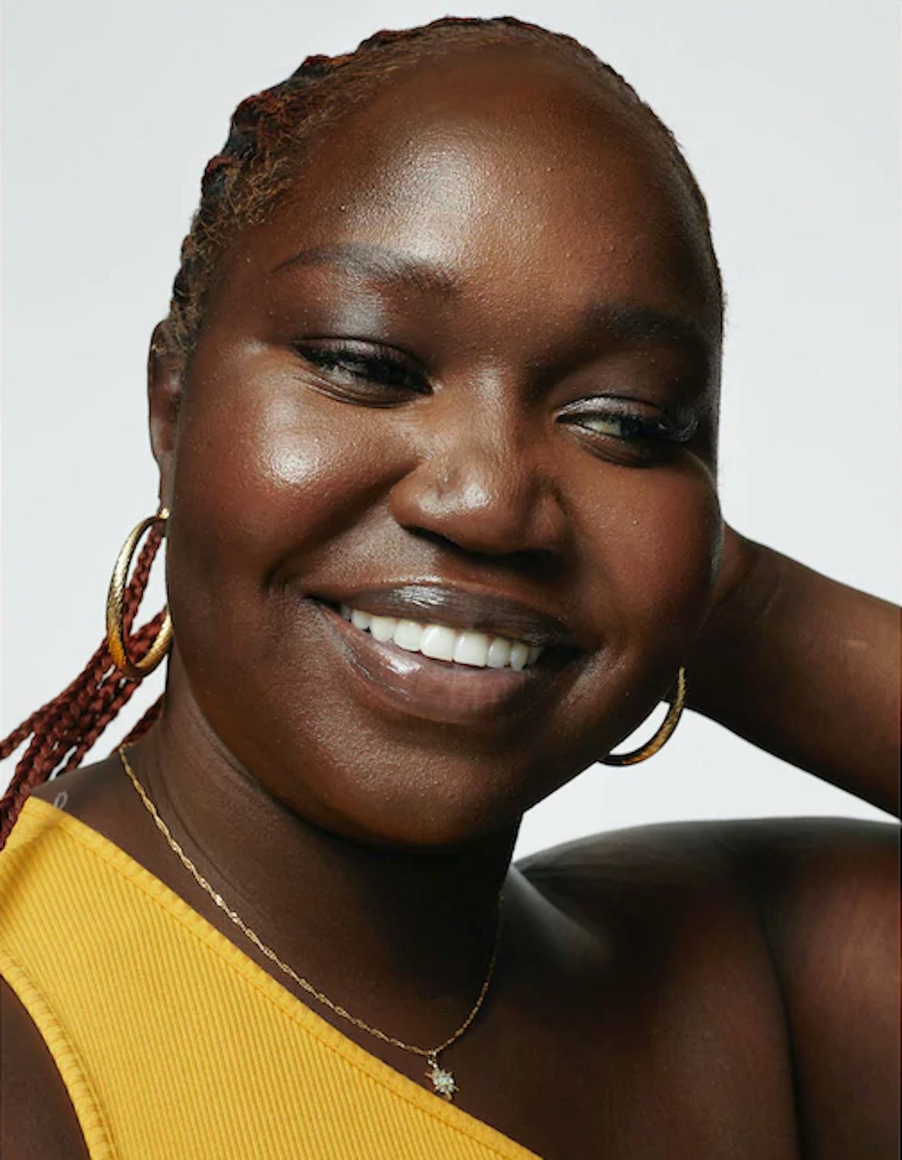 Black model smiling for Milk Makeup ad campaign in yellow shirt and braids.