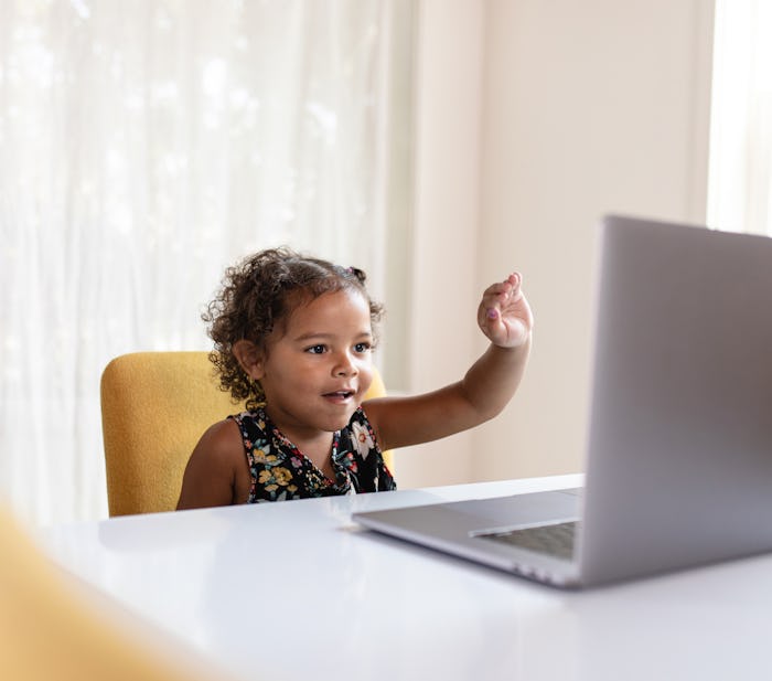 Little girl raising her hand in front of laptop screen