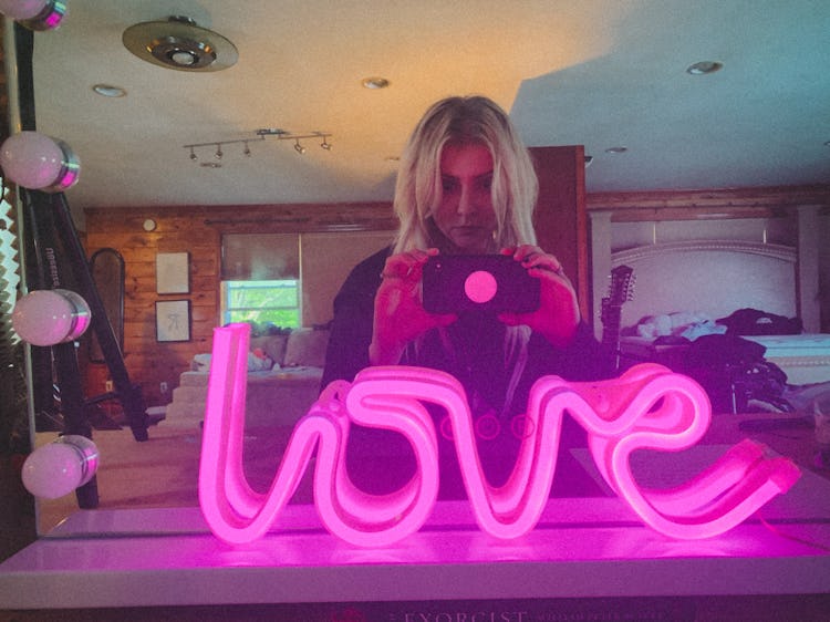 Taylor taking a selfie picture of a pink lightning sign with the word 'love' in front of a mirror